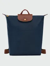 Mochila de diseño minimalista en color beige, con solapa y asa superior en cuero marrón texturizado. Cuenta con correas ajustables en color marrón y cierre principal.
