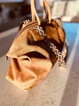 Bolso grande tipo tote de cuero color marrón gastado, con doble asa corta de madera y correa larga de tela estampada.