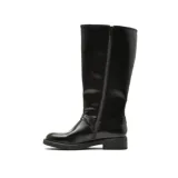 Bota de caña alta color negro, confeccionada en cuero sintético con acabado brillante. Presenta tres hebillas metálicas laterales, detalle de tachas plateadas a lo largo de la caña y una correa decorativa con argolla metálica en el tobillo. Cuenta con suela plana y taco bajo.