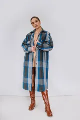 Tapado largo estilo camisa confeccionado en paño italiano, con diseño a cuadros en tonos de azul, gris y negro. Cuenta con cuello clásico, cierre frontal con botones, bolsillos con solapa en el pecho y mangas largas.