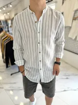 Camisa de lino blanca con rayas verticales negras, cuello mao y cierre frontal con botones marrones.