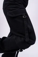 Pantalón cargo negro de jeans sin lycra, corte holgado y tiro alto. Cuenta con múltiples bolsillos laterales con solapa y cordones ajustables.