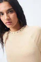 Remera blanca de manga corta con mangas ranglan y cuello redondo. El cuello tiene un bordado de estrellas negras alrededor.