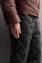 Pantalón de esquí acolchado con diseño de rombos, color negro. Presenta cintura elástica con cierre de botón a presión, bolsillos laterales con cremallera y bajos ajustables con cordón elástico.