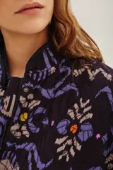Campera bomber acolchada con estampado geométrico en tonos violeta, azul y negro. Presenta cierre frontal con botones a presión, cuello redondo y puños elásticos.
