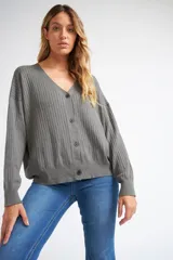 Cárdigan de tejido liviano con textura acanalada, cuello en V y cierre frontal con botones. Presenta mangas largas y un diseño clásico con detalle de grifa en cuero.
