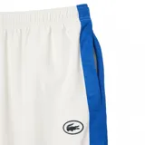 Pantalón de jogging blanco de corte recto con cintura elástica y cordón ajustable. Presenta una franja azul a lo largo de la pierna y el logo de Lacoste bordado en el muslo.
