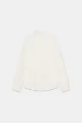 Camisa celeste de manga larga con cuello solapa y pliegues en los puños. Presenta cierre frontal con botones forrados al tono y bajo asimétrico.