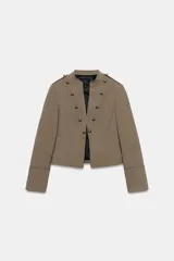 Blazer corto de estilo militar color tostado, con cuello redondo, manga larga y cierre frontal con ganchos metálicos. Presenta detalle de botones decorativos dorados en el frente y en los hombros, con costuras marcadas y forro interior a contraste.
