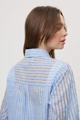 Camisa de manga larga con diseño de rayas verticales en tonos celestes, blancos y marrones, confeccionada en tejido semitransparente con cuello camisero y cierre frontal de botones.
