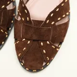 Sandalias chatitas de cuero en color marrón tostado, con diseño de tiras cruzadas en el empeine decoradas con tachas metálicas pequeñas. Cuenta con tira ajustable al tobillo mediante hebilla metálica y taco bajo.