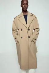 Trench largo de color negro con cuello de solapa, manga larga con trabillas ajustables y cierre frontal cruzado con doble botonadura. Cuenta con bolsillos delanteros de vivo, solapa cortavientos en el pecho y cinturón ajustable del mismo tejido.
