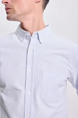 Camisa celeste a rayas verticales blancas, de corte clásico, con cuello abotonado, manga larga y bolsillo en el pecho.