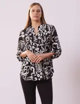 Blusa de gasa con estampado floral y botánico en blanco y negro, cuello a la base con escote en V y abertura central con botones, detalle de plisado frontal y mangas largas con presilla regulable.