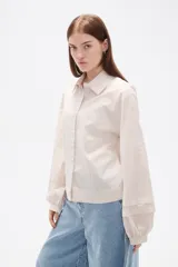 Camisa de algodón con estampado de rayas verticales finas en tonos beige y blanco, cuello clásico, cierre frontal con botones y mangas largas con puños anchos estructurados.