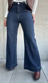 Jean de corte oxford con tiro alto, confeccionado en denim azul oscuro con costuras a tono. Presenta un diseño de pierna ancha y cierre frontal con botón metálico.