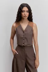 Chaleco corto marrón con estampado de rayas finas verticales, escote en V y cierre frontal con botones. Presenta detalles en los hombros y laterales en color tostado con efecto piel.