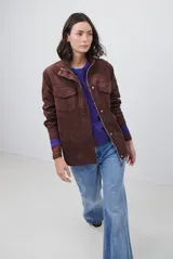 Chaqueta de gamuza en tono marrón oscuro, con cuello alto, cierre frontal con cremallera y botones a presión, bolsillos frontales con solapa y cinturón ajustable en la cintura.