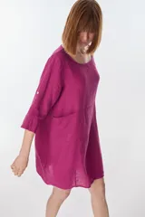 Vestido corto color beige de lino, con cuello redondo, corte oversize y mangas 3/4 con botón. Presenta bolsillos laterales.