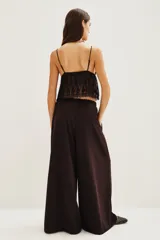 Pantalón de corte sastrero y pierna ancha, color marrón oscuro, con pinzas en la cintura y cierre frontal con lazo ajustable.