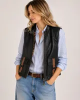 Chaleco de cuero negro con bolsillos frontales tipo cargo marrones con hebillas, cuello alto con broches y cierre frontal con cremallera.