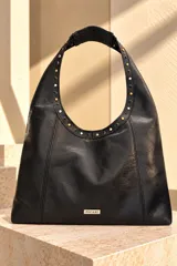 Cartera tipo hobo de cuero sintético negro, con detalles de tachas metálicas en las asas y placa con el logo de la marca en la parte frontal inferior.