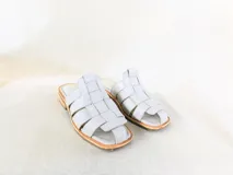 Sandalias bajas de cuero sintético color gris claro, con diseño de tiras entretejidas y suela plana.