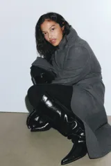 Abrigo midi de paño en color gris oscuro, con solapas de muesca, cierre oculto con botones a presión y cinturón ajustable a la cintura. Presenta bolsillos laterales discretos, abertura trasera y forro interior.