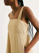 Vestido corto de color beige con escote cuadrado, tirantes anchos y corte recto con bolsillos laterales.