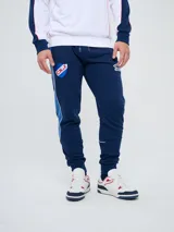 Pantalón de jogging azul marino Umbro del Club Nacional de Football, con cordón ajustable en la cintura, puños elastizados en los tobillos y bandas laterales en tonos de azul. Cuenta con el escudo del club en una pierna y el logo de la marca en la otra.