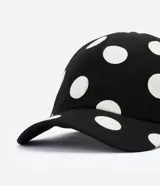 Gorra de sarga de algodón con visera curva, ojales bordados y estampado de lunares, con cierre posterior ajustable con hebilla metálica.
