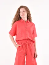 Camisa de lino color rojo, de corte holgado, con cuello clásico, cierre frontal de botones y mangas cortas con dobladillo. Presenta dos bolsillos frontales tipo parche.