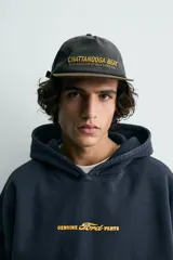 Gorra de algodón negra con visera plana de color marrón oscuro. Presenta bordado frontal en hilo dorado con el texto "CHATTANOOGA BEAT THE LANGUAGE OF JAZZ SINCE 1920".