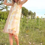 Vestido corto sin mangas, con estampado de hojas en tonos beige y verde, y falda color lila con detalle de flecos en el ruedo.