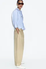 Pantalón de tiro alto en color beige, con pinzas delanteras, bolsillos laterales y bajo con vuelta. Presenta un cierre frontal con cremallera, botón interior y gancho.