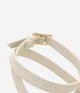 Sandalia plana tipo salomé color beige, con tiras finas, cierre con hebilla lateral y detalle decorativo dorado en la parte frontal. Cuenta con una suela de plataforma baja en tono madera.