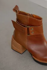 Bota corta de cuero negro con acabado combinado mate y charol. Presenta una tira decorativa con tachas metálicas y hebilla en el tobillo, tacón cuadrado robusto y suela con plataforma.