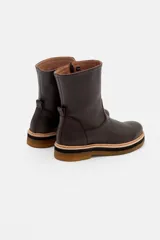 Bota de caña media confeccionada en cuero vacuno texturizado color marrón oscuro. Presenta un diseño minimalista con costuras reforzadas, tirador trasero y una suela de plataforma plana con capas en tonos beige, negro y suela.