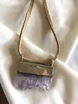 Collar con dije de piedra amatista irregular y engarce plateado, con cordón de cuero marrón.