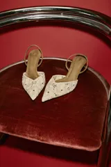 Zapato de tacón medio fino y destalonado, color beige con cuerpo de tejido bordado con motivos florales, punta fina y tira trasera elástica.