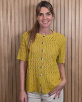 Cardigan de punto calado color mostaza, de manga corta y cuello redondo, con cierre frontal de botones.
