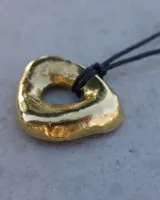 Collar con dije de forma irregular en tonos dorados y plateados, suspendido de un cordón doble de algodón negro.