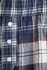 Pantalón largo de tejido suave con estampado a cuadros en tonos azul, marrón y blanco. Tiene elástico en la cintura, cierre decorativo con botones y bolsillos laterales.