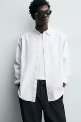 Camisa de corte regular fit confeccionada en tejido de algodón con diseño de rayas verticales. Presenta cuello abotonado, manga larga con puños abotonados, bolsillo plastrón en el pecho y cierre frontal con botones.