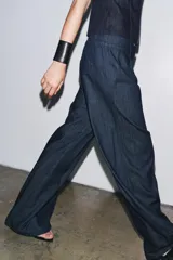 Pantalón culotte de denim azul oscuro, tiro medio, con cintura elástica en la parte trasera, bolsillos laterales y pinzas delanteras. Cierre frontal con cremallera, botón y ganchos metálicos.