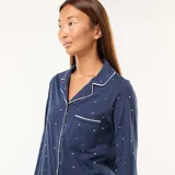 Pijama largo de dos piezas azul marino con estampado de estrellas blancas y ribetes blancos. Incluye camisa de manga larga con cuello y botones, y pantalón largo de corte recto.