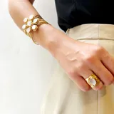 Pulsera artesanal de bronce con diseño de flor central compuesta por piedras blancas de forma ovalada. Presenta una estructura de múltiples hilos metálicos que forman un brazalete tipo cuff.