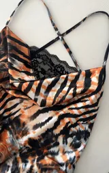 Minivestido ajustado con estampado animal print en tonos naranja, marrón y negro. Diseño con escote drapeado con detalle de encaje negro y tirantes finos.