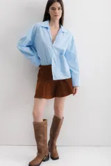 Camisa blanca de algodón, de corte holgado, con cuello clásico, mangas largas con puños anchos y un bolsillo de parche en el lateral.