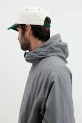 Campera rompevientos de nylon color gris oscuro, con forro de malla. Presenta cierre frontal con protección para el mentón, capucha ajustable con cordón, bolsillos laterales y un bolsillo interior, todos con cierre. Los puños y el bajo tienen elástico revestido.